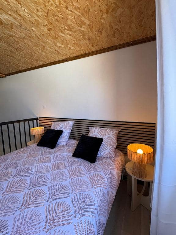 Chambre à lit double au bas, plafond OSB brut et lampes de chevet en osier · © Au Pied des Sources by K