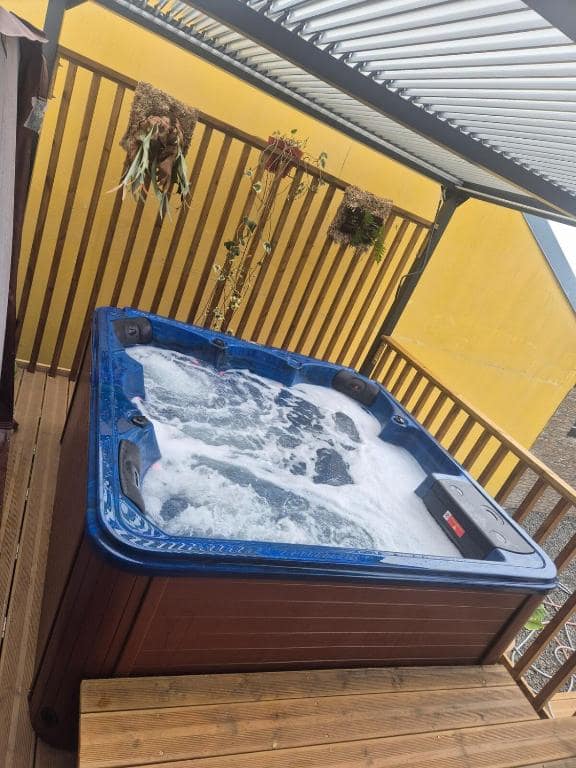 Jacuzzi sur deck bois, paroi jaune · © Au Pied des Sources by K