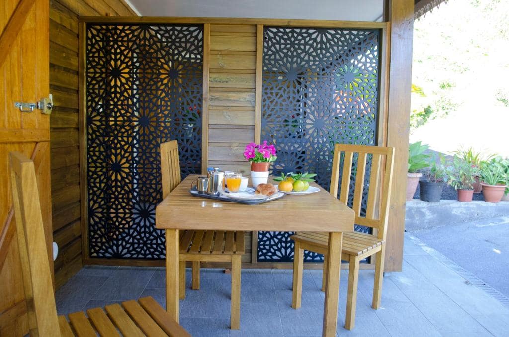 Terrasse petit-déjeuner, table bois derrière panneaux ajourés · © Bec Roz'