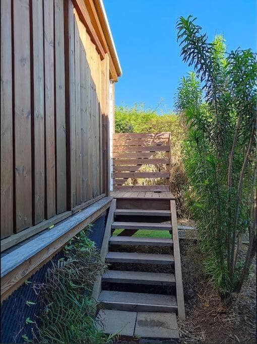 Escalier extérieur bois vers l'entrée, façade en tasseaux · © Les Songes