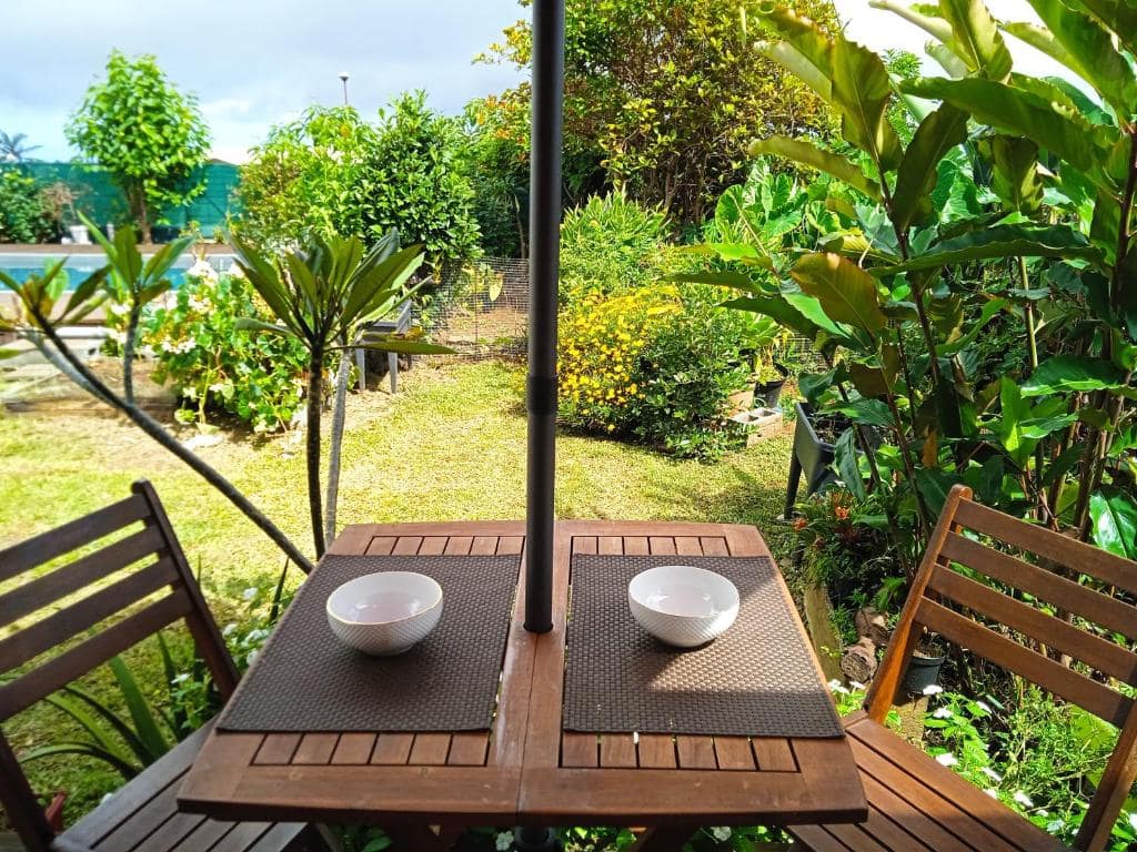 Table extérieure avec deux bols et parasol dressé face au jardin · © Bungalow Maïdo