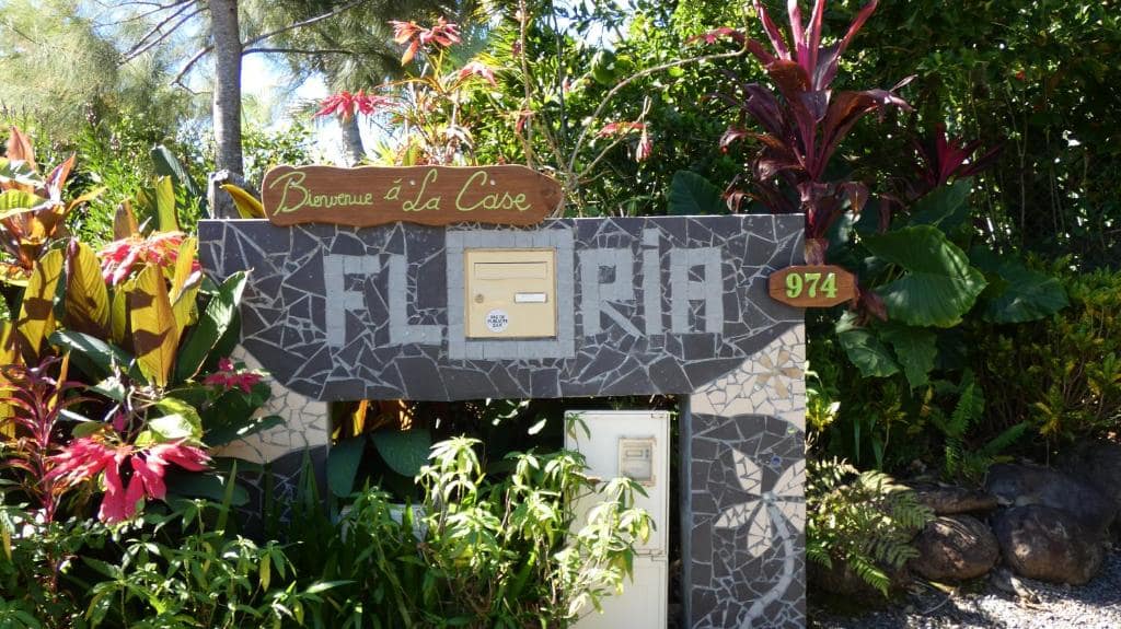 Portail mosaïque à l'enseigne Floria dans un massif fleuri · © La Case Floria