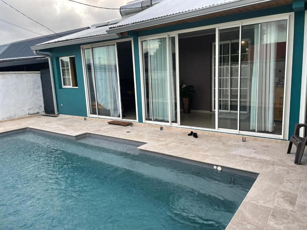 Piscine bordée d'un dallage travertin devant la villa bleu canard · © Chambre dans notre Villa avec Piscine
