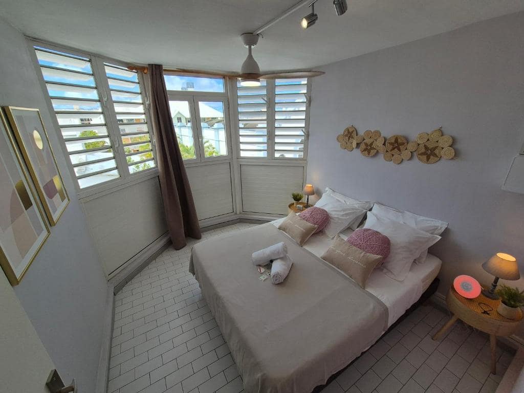 Chambre principale, vitres à jalousies, décor rotin mural · © Cœur Citadin