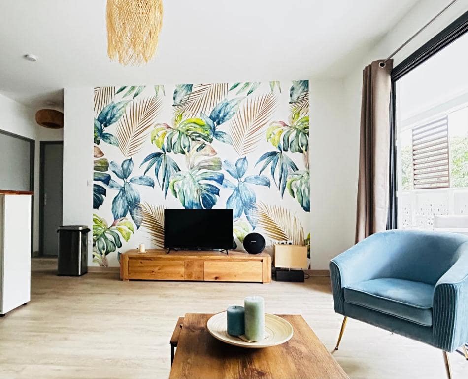 Salon télévision avec fauteuil bleu et fresque tropicale · © Cosy Sand