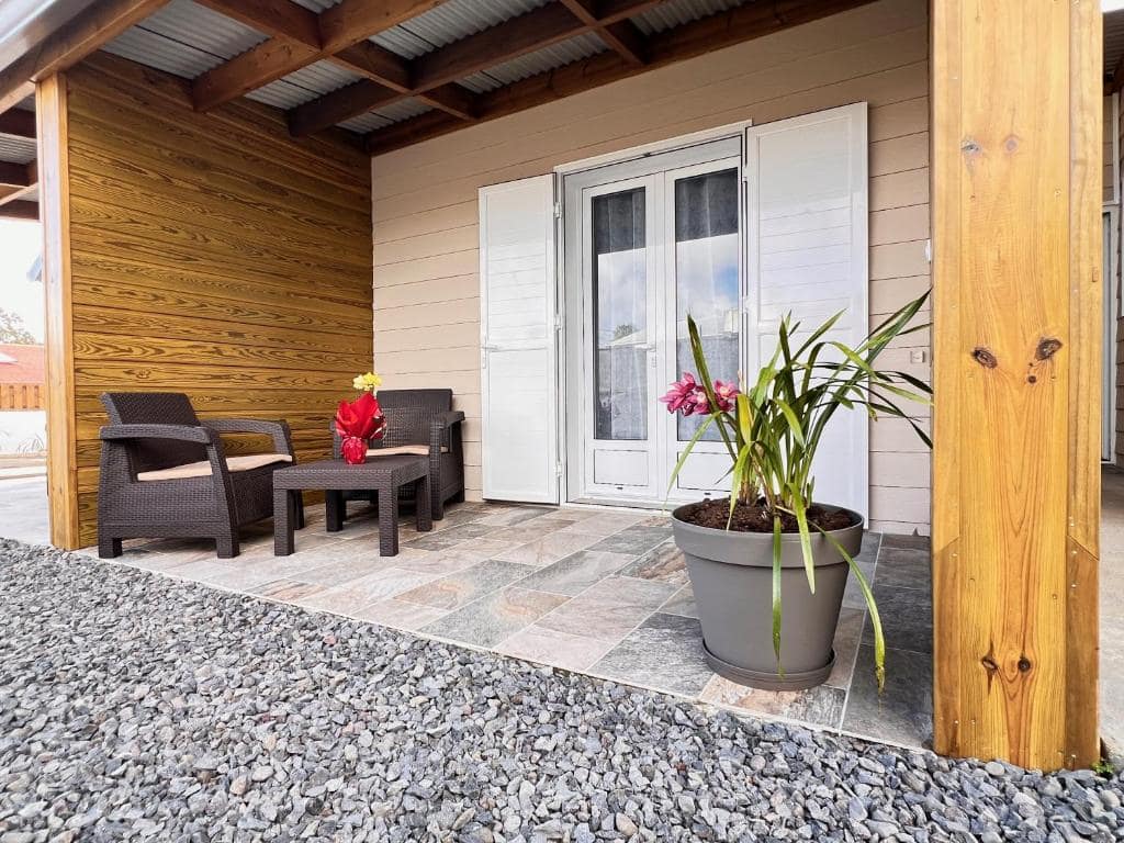 Terrasse couverte, fauteuils en résine et plantes fleuries · © L'Enclos du Volcan