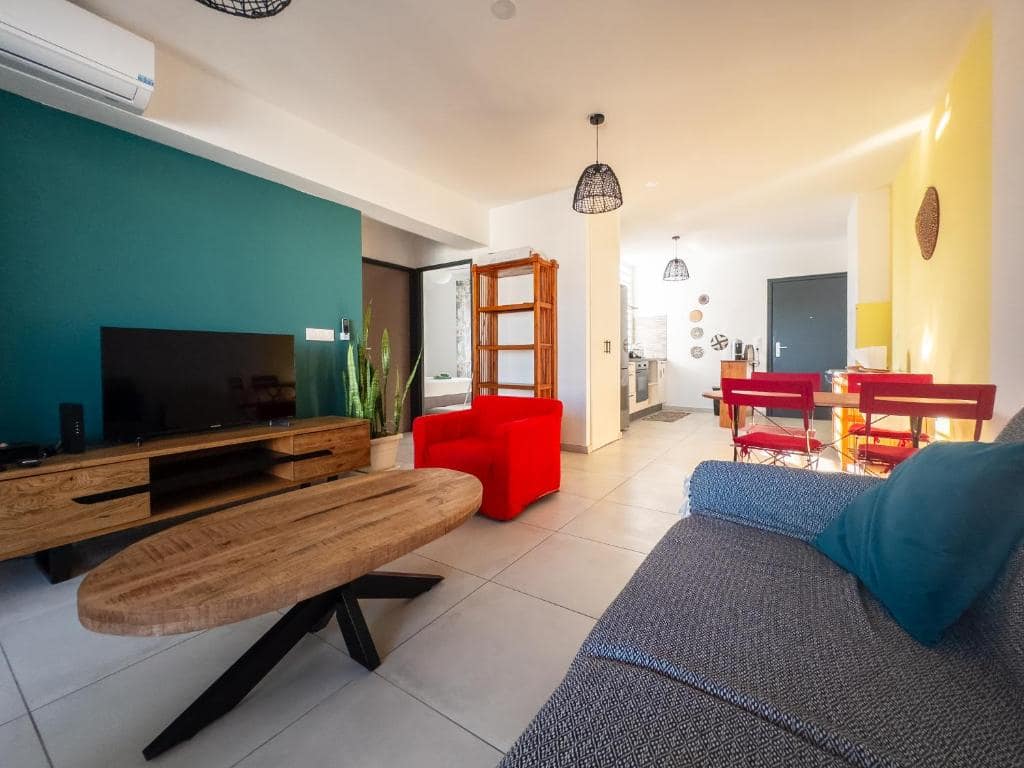 Séjour ouvert sur cuisine, mur vert et fauteuil rouge · © Évasion Saint-Leu