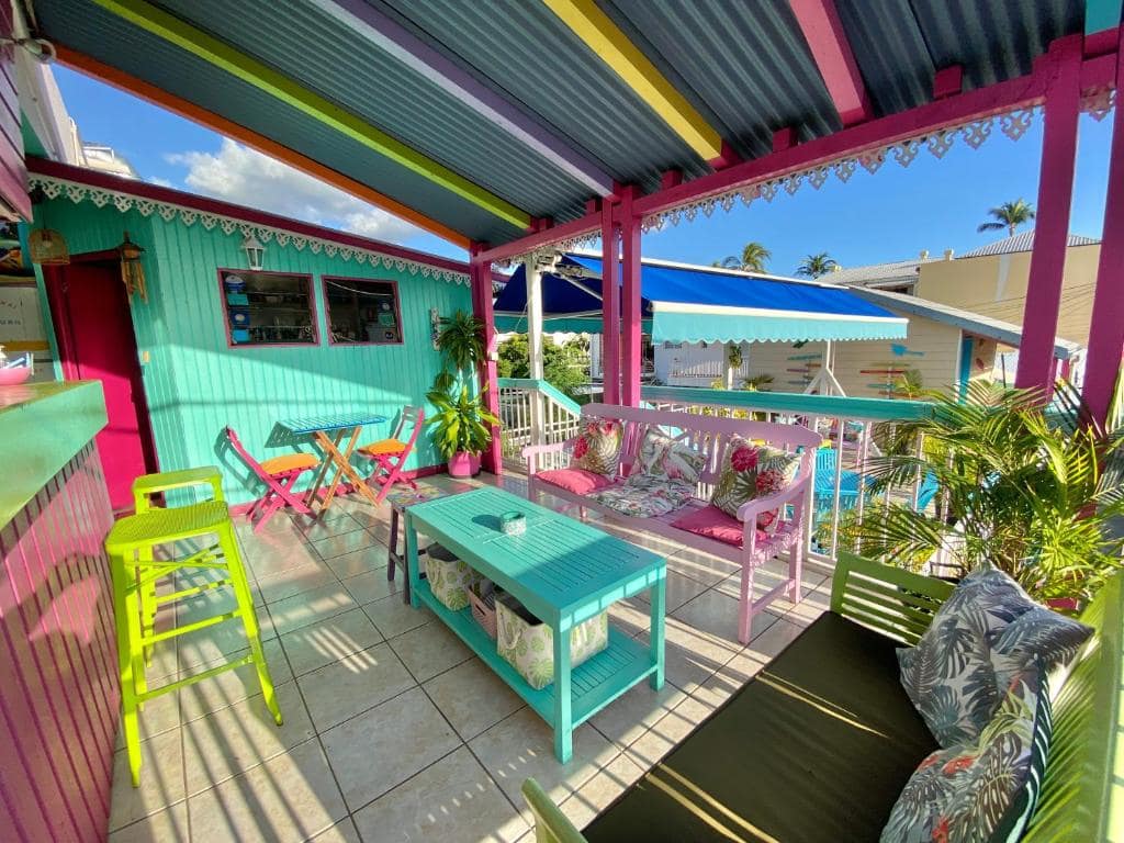 Terrasse commune colorée, mobilier créole rose et bleu · © Hôtel De la Plage