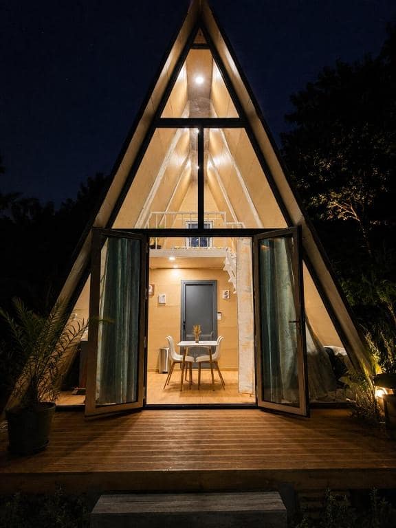 Façade éclairée de nuit, portes ouvertes sur la terrasse en bois · © Kaz triang
