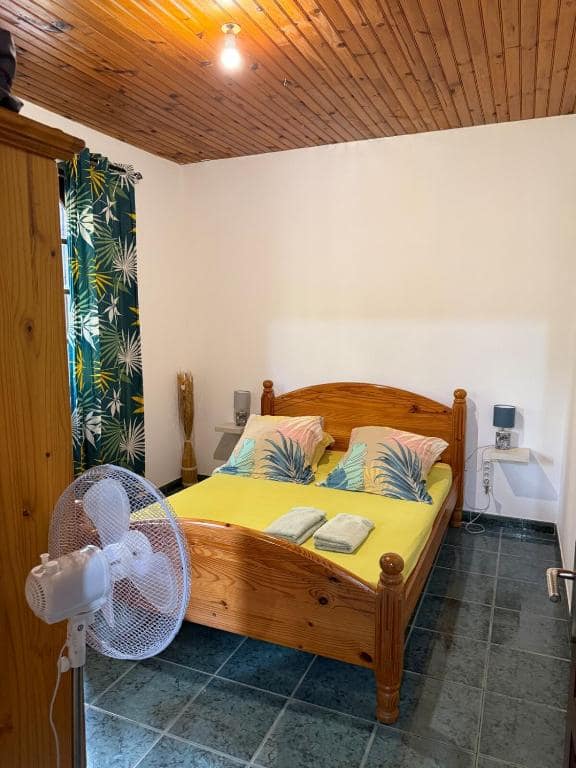 Chambre avec plafond bois vernis, lit ventilateur et rideau tropical · © Kaz'A Olymp