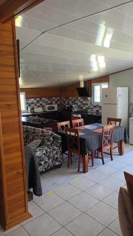 Séjour avec grande table, cuisine et frigo au fond · © La cacaoyère