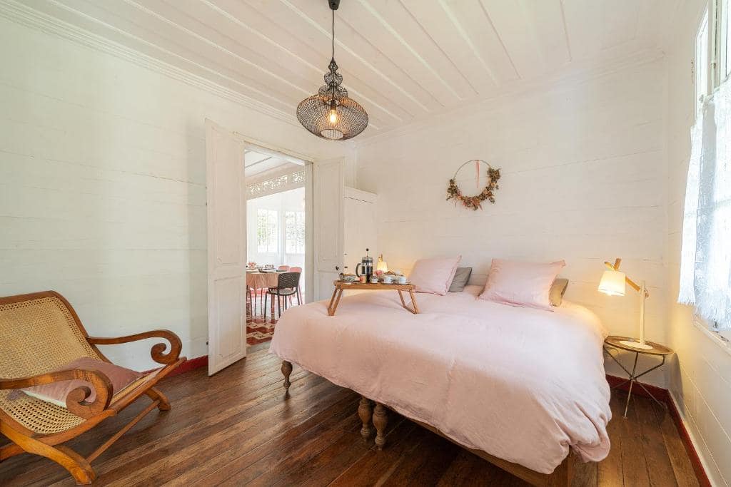 Chambre créole boisée blanche, lit double et fauteuil en rotin ancien · © La Villa Blanche