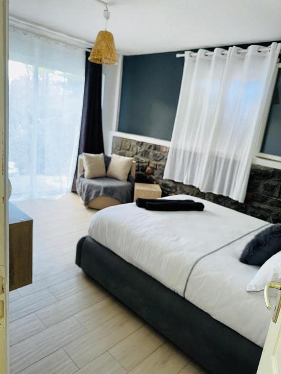 Chambre couple à grand lit, baie vitrée et banquette sur mur bleu · © LaKaz à Eva