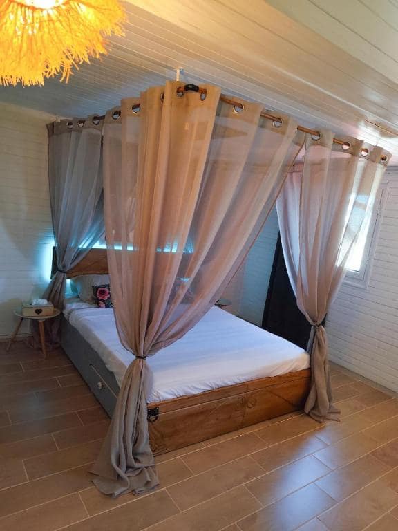 Chambre à baldaquin voilée sous suspension jaune en osier · © l'Antre Temps