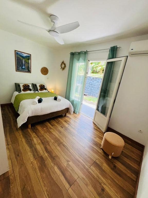 Chambre avec plaid vert, ventilateur de plafond et tableau cascade · © Le Calouni