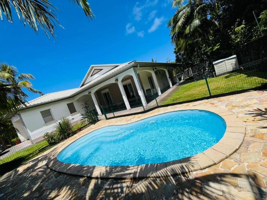 Villa créole à colonnes et bassin bleu vus depuis la dalle · © Le Calouni
