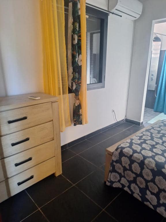 Chambre avec commode bois, rideaux jaunes et voilage à motif floral · © L'écrin de douceur