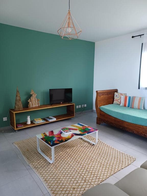 Salon avec canapé banquette bois, mur d'accent vert, TV · © Les jumelles