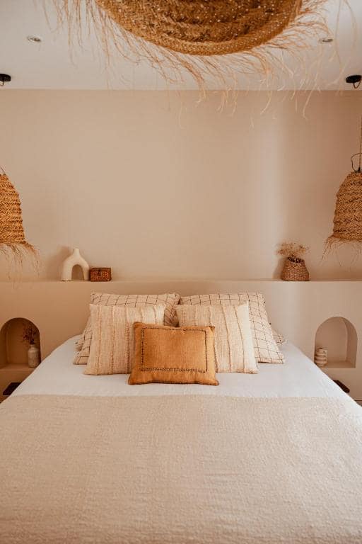 Chambre aux tons sable, tête de lit voûtée et suspensions en osier · © Lodge des palmiers - jacuzzi