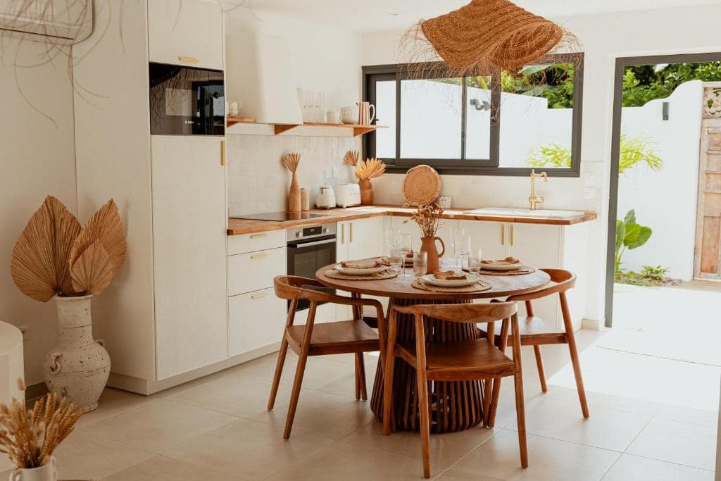 Cuisine ouverte sur salle à manger, chaises bois et porte-fenêtre sur jardin · © Lodge des palmiers - jacuzzi