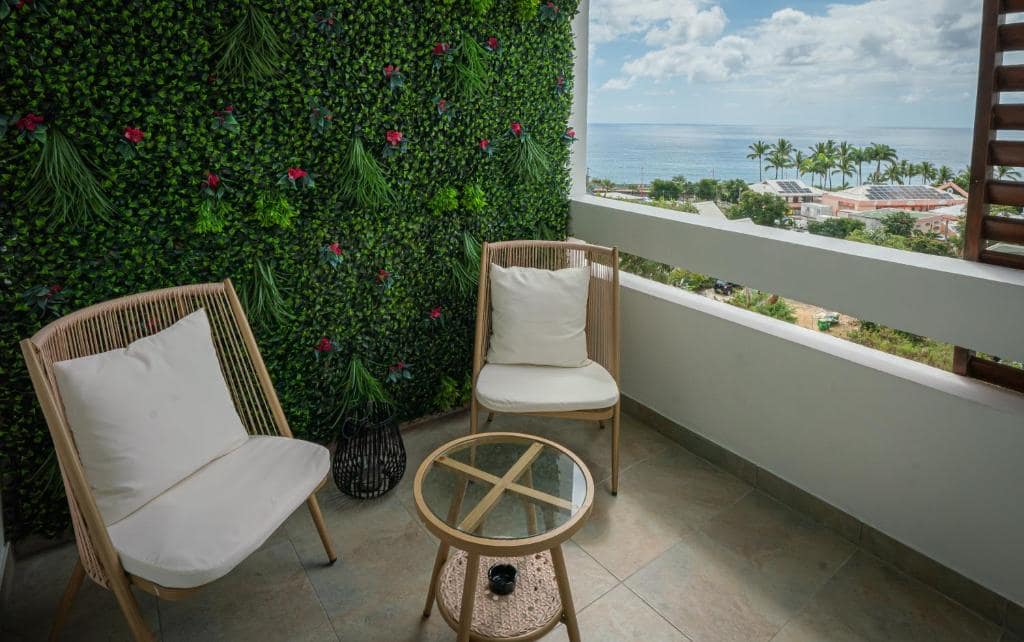 Balcon avec mur végétal fleuri, fauteuils rotin, vue océan · © Mafat'appart