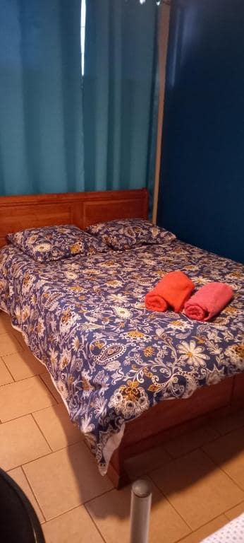 Chambre carrelée avec couvre-lit bleu à motif ethnique et serviettes rouges · © Maison de Vacances à Bras-Panon