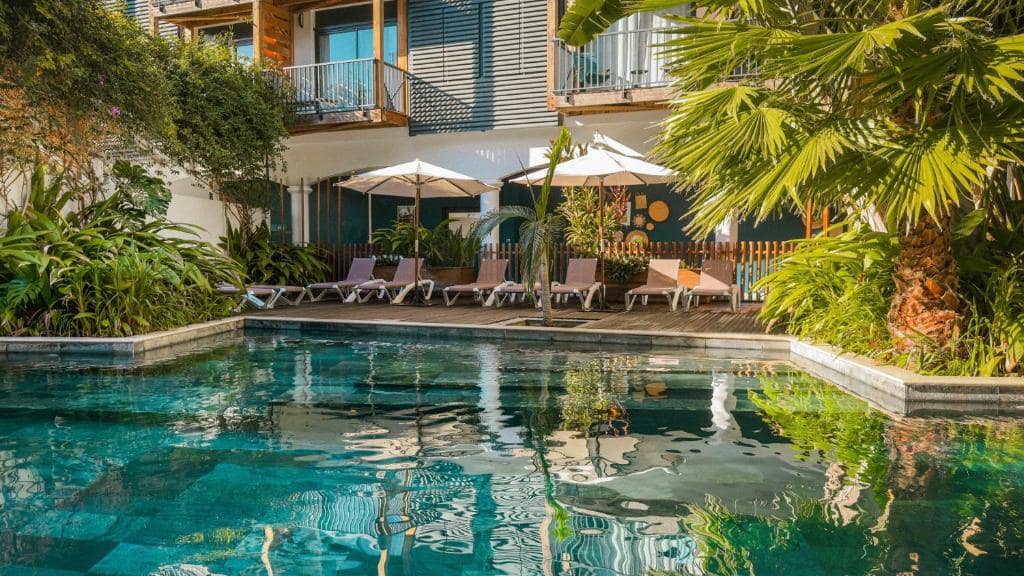 Piscine extérieure sous palmiers et façade bardée · © Santa Apolonia