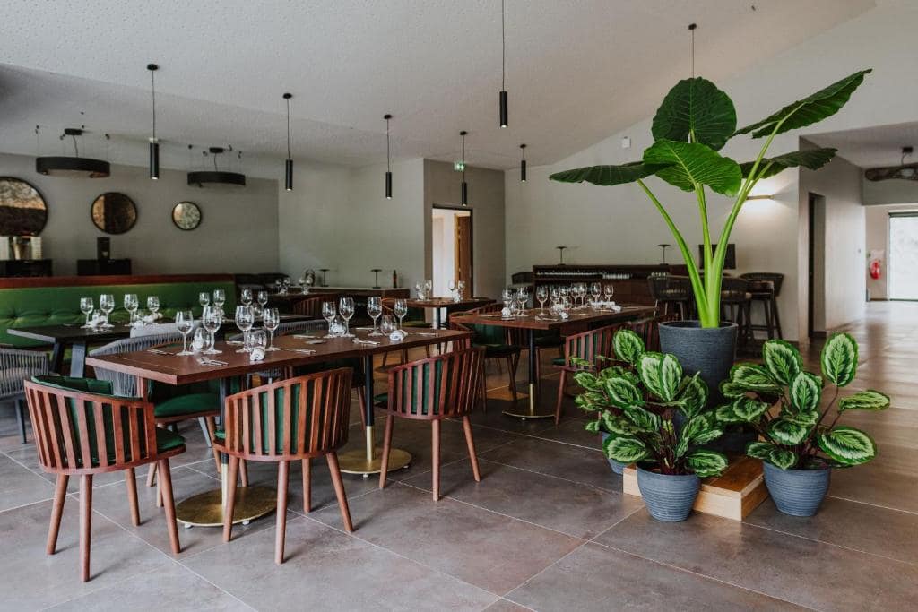 Salle du restaurant, tables dressées entre grandes plantes vertes · © Sarana Hôtel & Spa