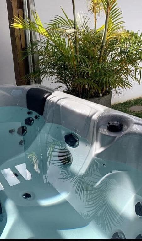 Jacuzzi extérieur en gros plan avec palmier en pot au-dessus · © Sweet Moka