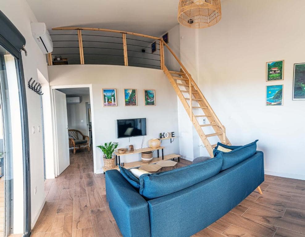 Séjour double hauteur avec mezzanine, canapé bleu et escalier bois · © Sweet Moka