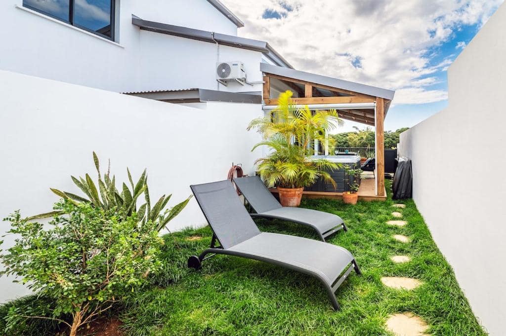 Jardin latéral, transats sur pelouse et jacuzzi sous pergola en fond · © Sweet Moka