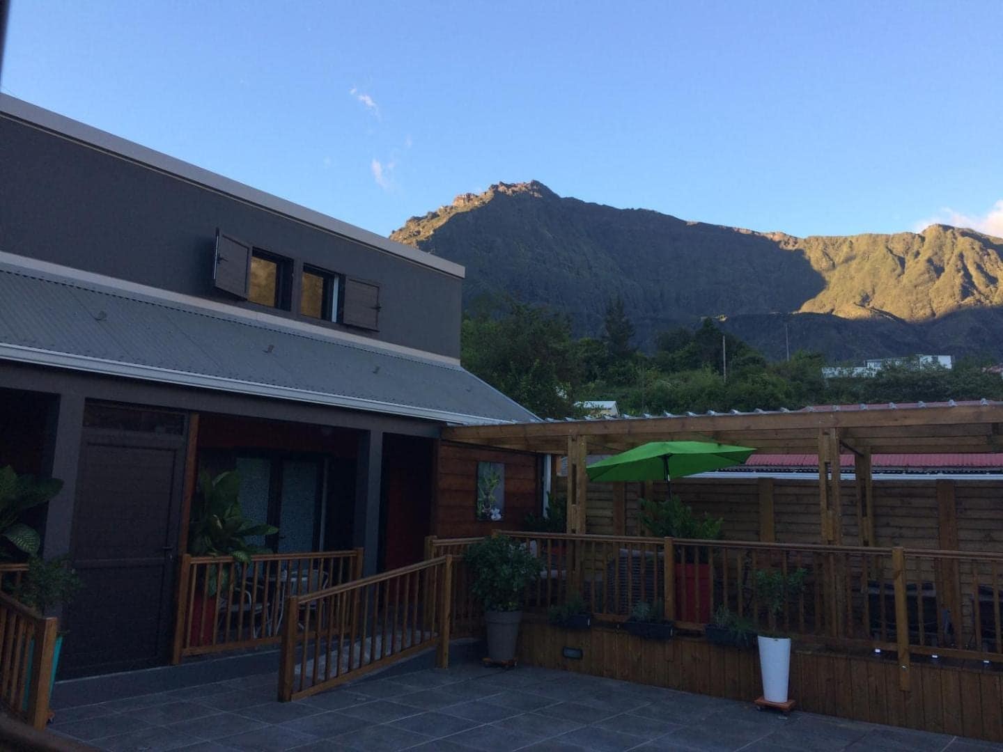Terrasse en bois et parasol vert, montagne au fond · © Ti Fleur Aimée