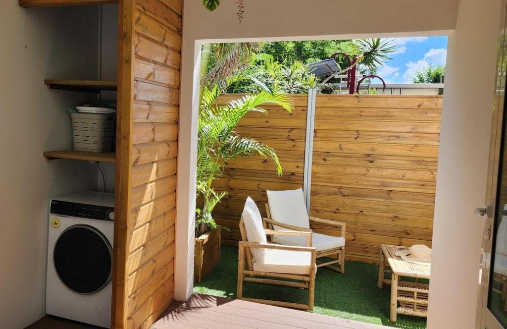 Terrasse extérieure avec fauteuils bambou et lave-linge en desserte · © Ti Kaz Angelyn