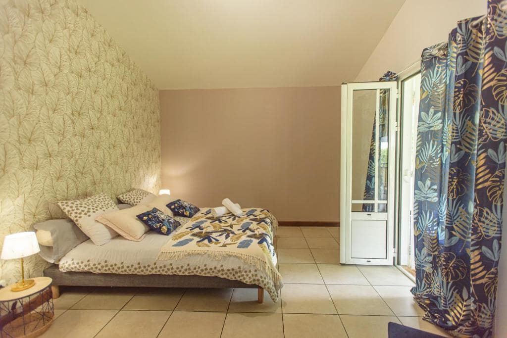 Chambre avec grand lit, tapisserie feuillage et rideaux monstera · © Ti Kaz Bibass