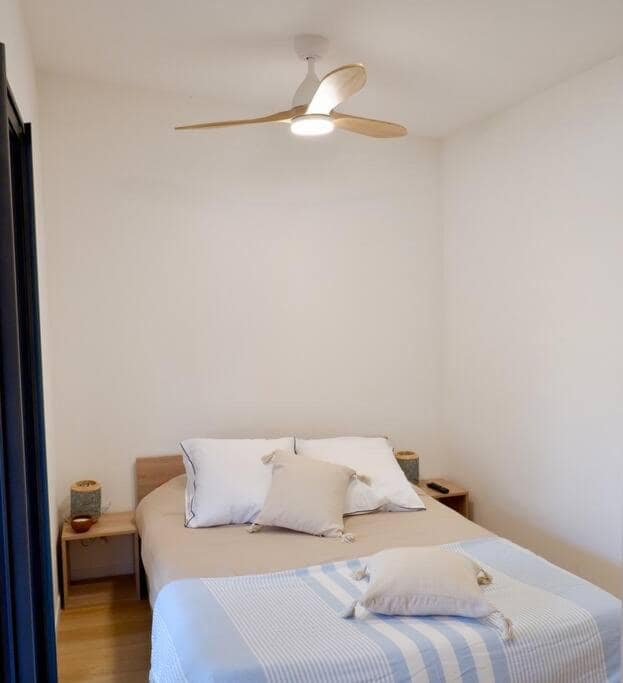 Chambre lit blanc et bleu sous ventilateur à pales bois · © Ti Kaz