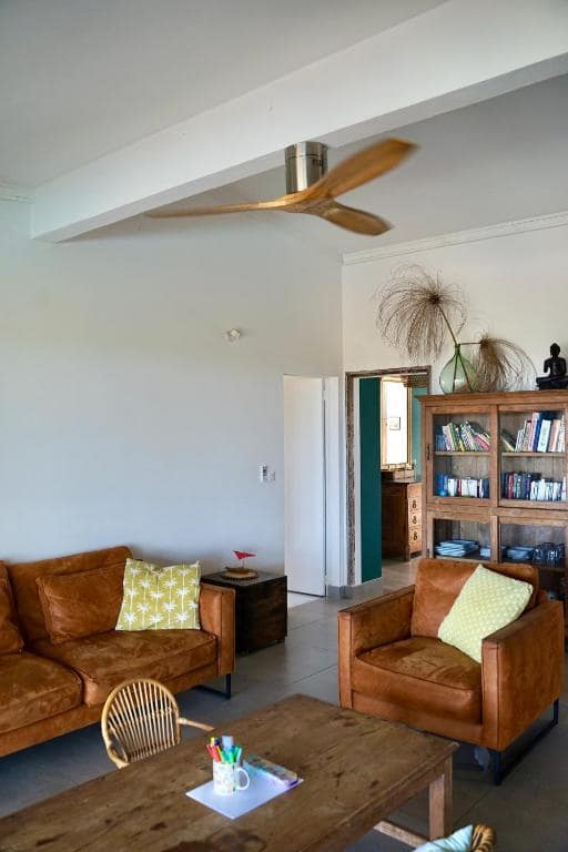 Séjour avec canapé cuir et grand ventilateur à pales bois · © Villa Acacias