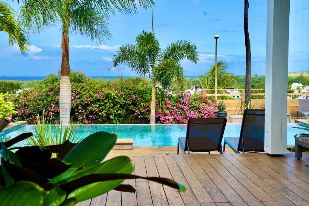 Deck de piscine bordé de bougainvilliers face à la mer · © Villa Acacias