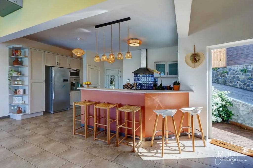 Cuisine ouverte, îlot orange et tabourets en osier · © Villa Amara