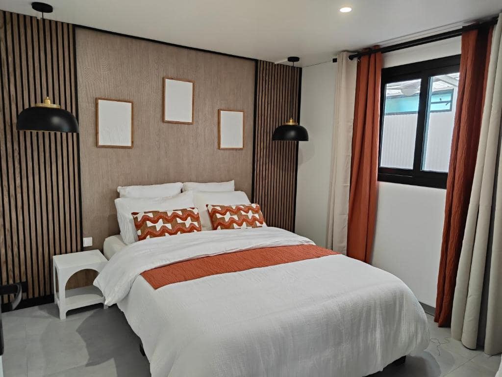Espace couple au niveau bas, tête de lit tapissée et rideaux orangés · © Villa au coeur de marius