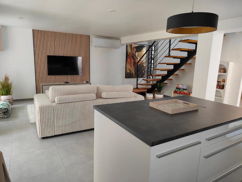 Salon ouvert sur cuisine, escalier bois au fond · © Villa au coeur de marius