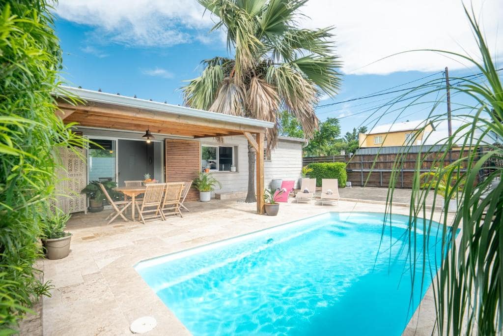 Piscine bordée de travertin devant la villa en bois blanc · © Les Lataniers