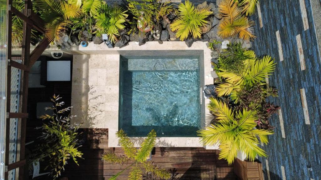 Petite piscine vue du dessus, cernée de palmiers et de galets · © Villa Loret
