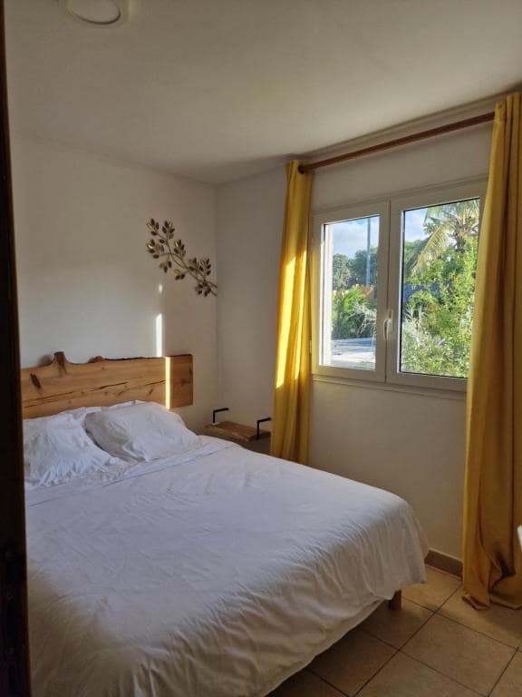 Chambre bois clair avec rideaux jaunes et grande baie vitrée · © La Villa'mie