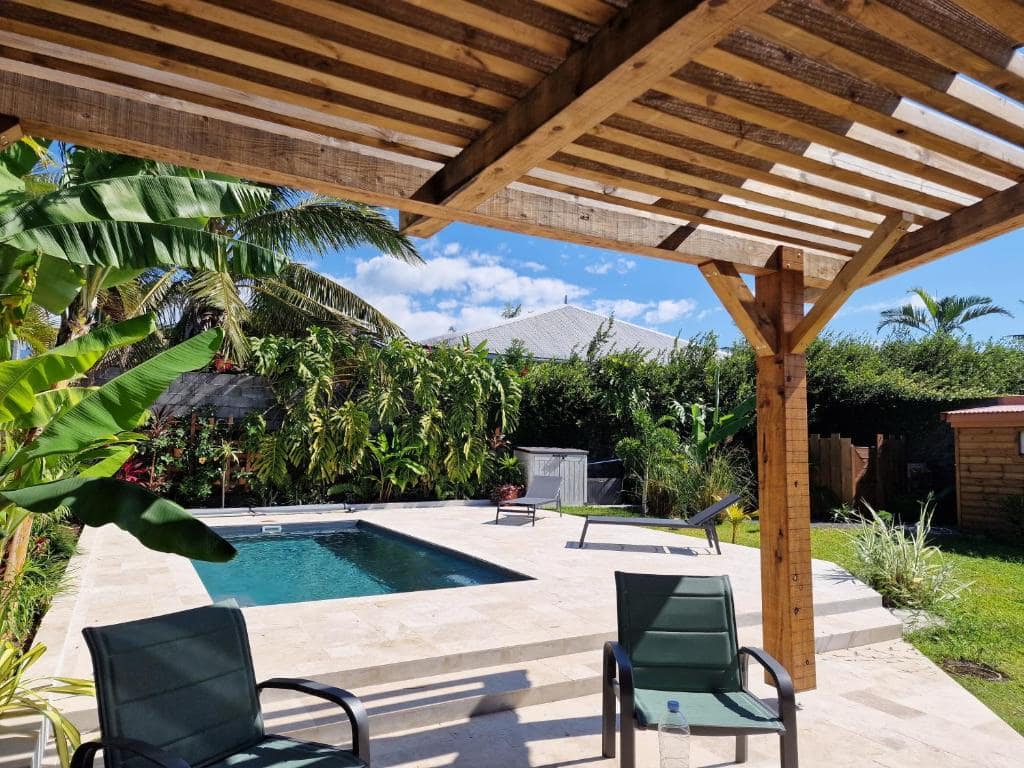 Pergola bois au-dessus de la piscine avec chaises longues face au jardin · © La Villa'mie