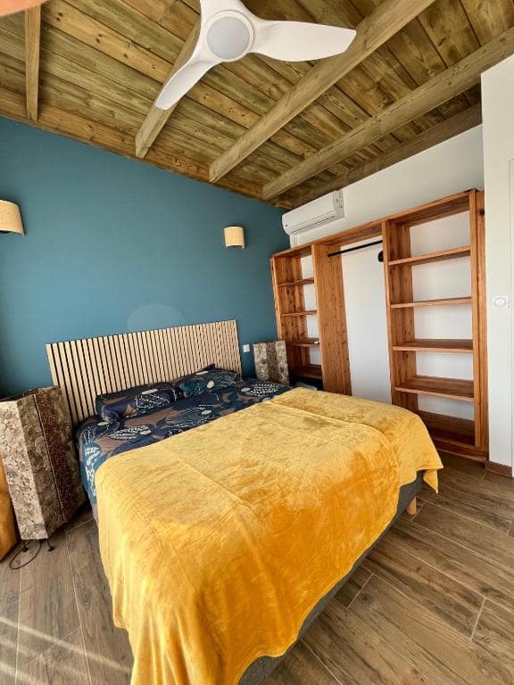 Chambre couvre-lit jaune, plafond bois et grand dressing ouvert · © Villa neuve vue mer