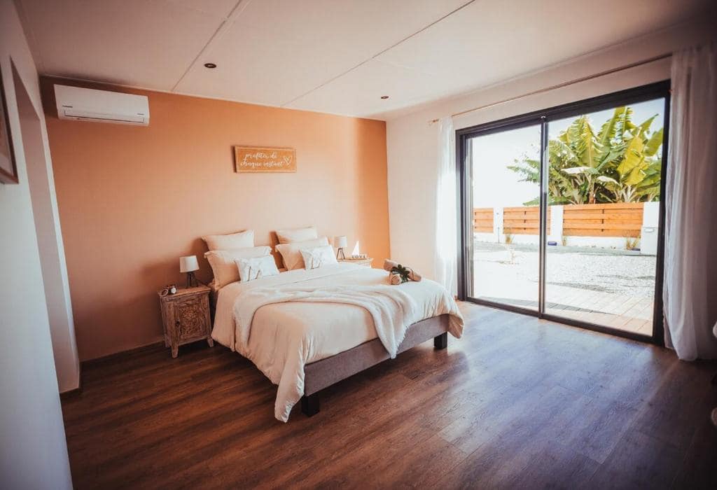 Chambre au mur orange avec grande porte-fenêtre sur bananiers · © Villa O Ptit Bonheur