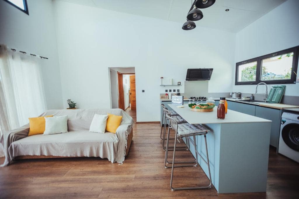 Séjour double hauteur avec cuisine îlot, tabourets et canapé blanc · © Villa O Ptit Bonheur