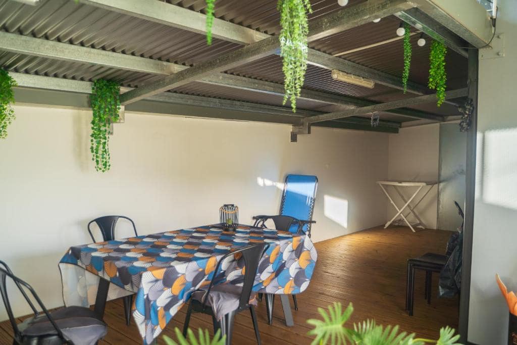 Terrasse couverte avec table nappée et suspensions vertes · © Villa de la Rivière du Mât