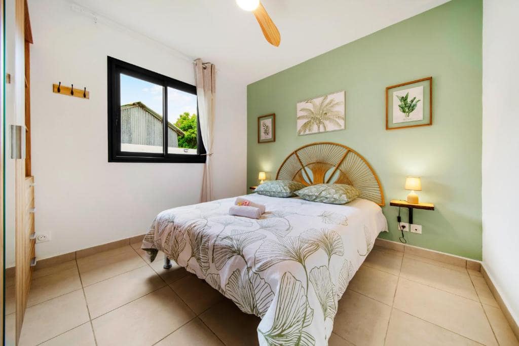 Chambre au mur vert avec tête de lit rotin en éventail · © Villa Takamaka